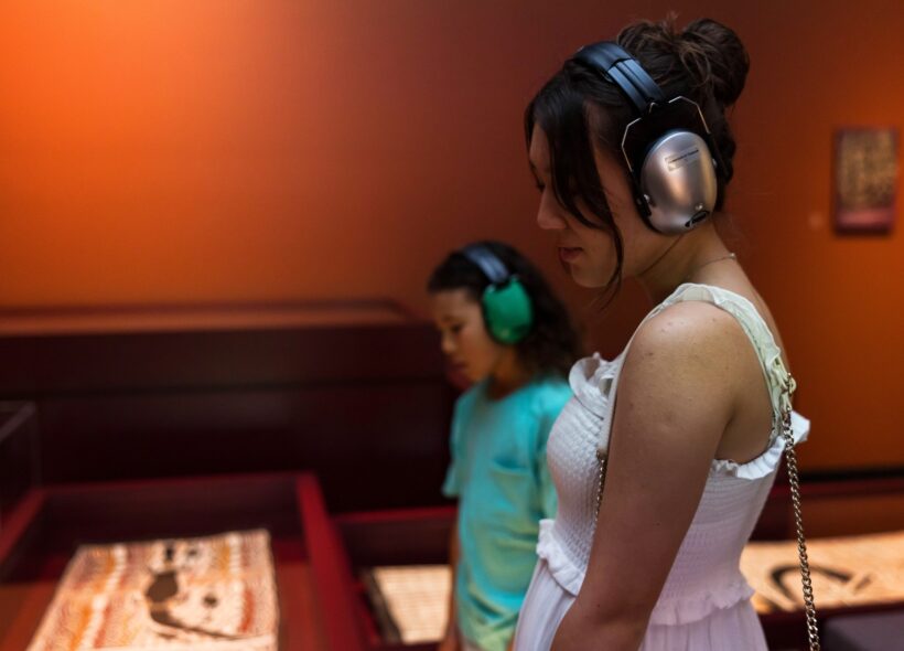 Two young people wear ear protection in a gallery space with muted lighting.