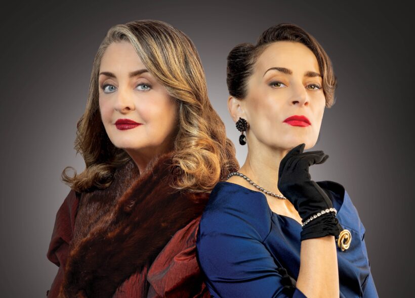 Two elegantly dressed women stand back-to-back against a dark gradient background. One wears a red dress with a fur stole, and the other a blue dress with gloves. Both have confident, poised expressions.
