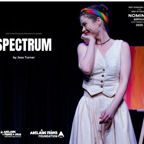 Promotional poster for the stage show “SPECTRUM” by Jess Turner. A smiling performer stands on a dark theatre stage, wearing a cream vintage-style dress with buttons down the front, black stockings, and black shoes. She has her hair in a bun with a rainbow headband and rests her hand against her cheek in a playful, bashful pose.  Behind her is an easel displaying a canvas painted in warm gradient tones (red, orange, yellow).  Text on the image reads: “Jess Turner & Sunburnt Productions Co. present SPECTRUM by Jess Turner.” “Best Emerging Artist and Best in Theatre Nominee – Sydney Fringe Festival 2025.”  Logos along the bottom include Sunburnt Productions, Adelaide Fringe 2026 (adelaidefringe.com.au), and Adelaide Fringe Foundation.