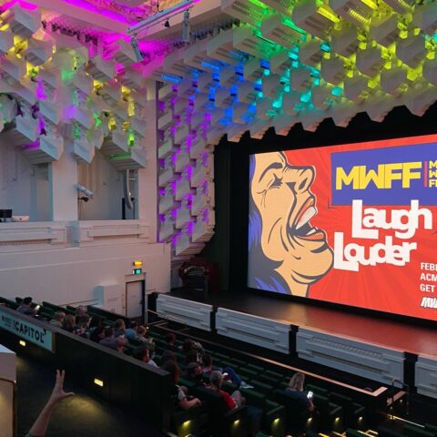 A photo of the Capitol theatre with an audience and an image on the big screen reading 