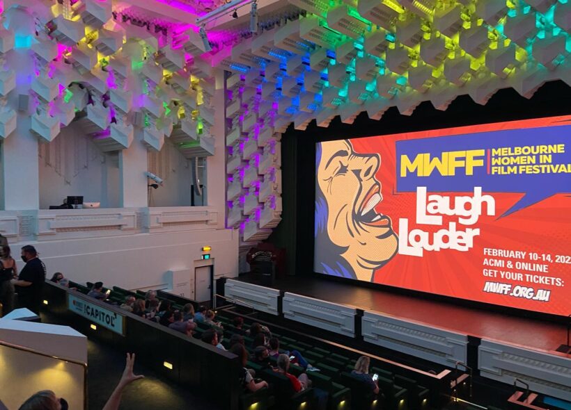 A photo of the Capitol theatre with an audience and an image on the big screen reading 
