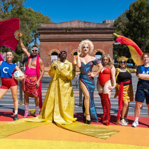 Promo image of artists posed on the rainbow walkway outside Qtopia Sydney
