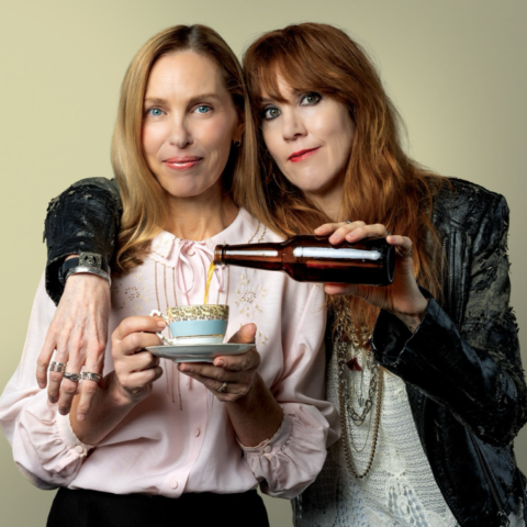 Two women, one dressed in black leather holding a beer and the other dressed in pink with a coffee