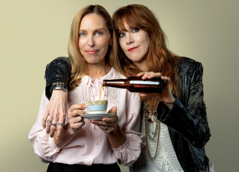 Two women, one dressed in black leather holding a beer and the other dressed in pink with a coffee