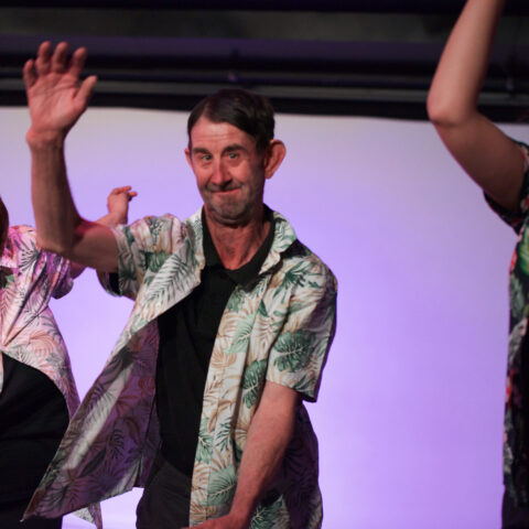 Adults perform during a Restless Dance Theatre end-of-year showing. Three adults wearing Hawaiian shirts while dancing on stage.