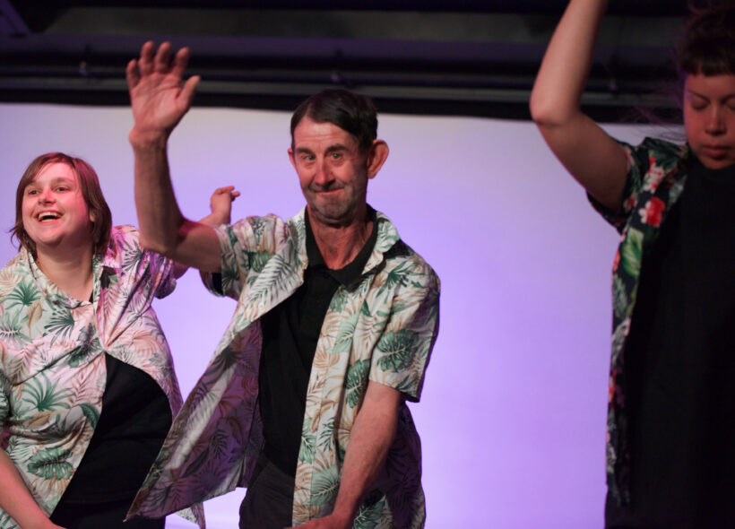 Adults perform during a Restless Dance Theatre end-of-year showing. Three adults wearing Hawaiian shirts while dancing on stage.