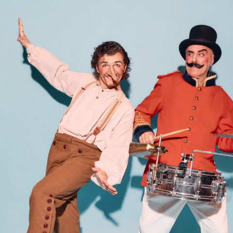 Man made out of wood and pinocchio's nose next to a red coat man in a toop hat and big moustache 