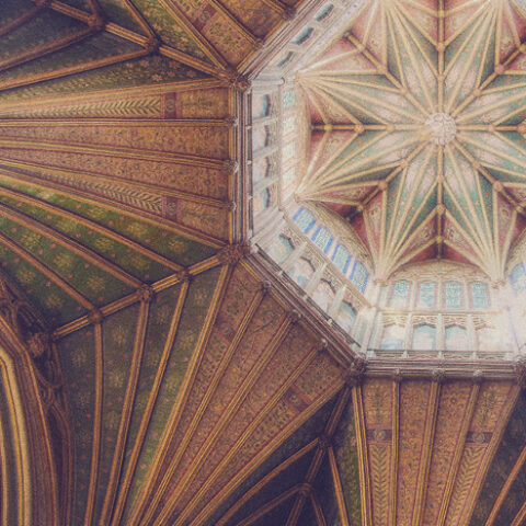 Ornate cathedral ceiling with intricate geometric patterns, stained glass windows, and warm tones of green and brown, conveying a sense of awe.
