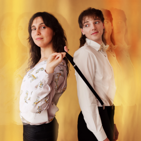 Two people stand back-to-back against a warm, blurred background. One wears a patterned shirt. The other is in a bow tie and suspenders, looking to the side. 