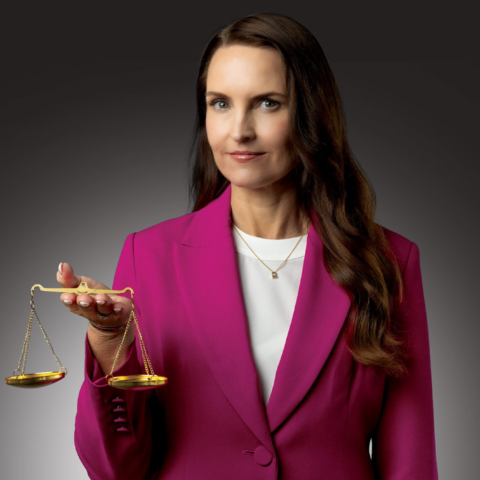 A professional woman in a pink suit holds the scales of justice 