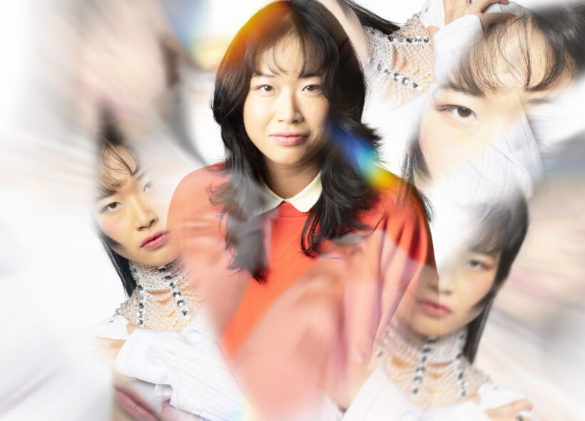 A woman in an orange sweater is centered, surrounded by multiple blurred and overlapping images of herself against a white background.