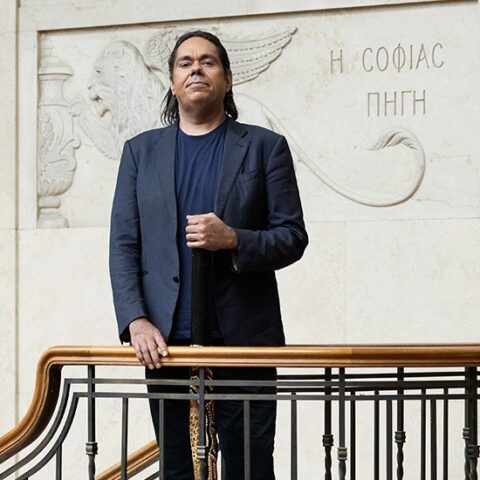 A man stands confidently on a staircase holding a yidaki 