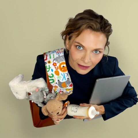 A woman stares up at the camera holding a laptop, baby blanket, plush toys and baby bottle.  