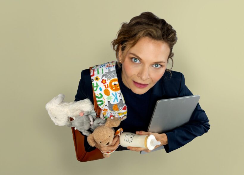 A woman stares up at the camera holding a laptop, baby blanket, plush toys and baby bottle.  