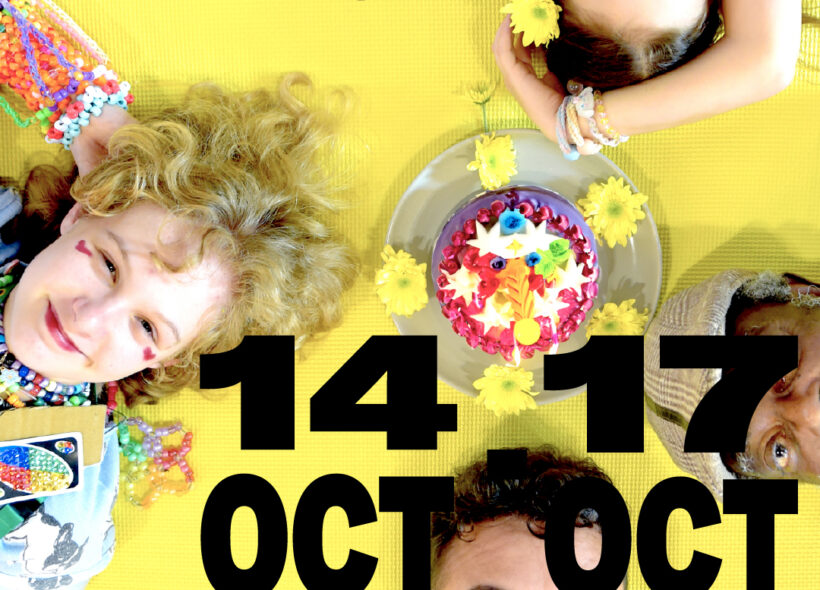 Four people across a range of ages are laying around a cake while looking up at the camera