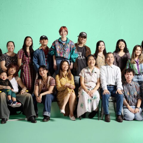 Very big cheerful group portrait of Vietnamese family and friends, all smiling against a green background 