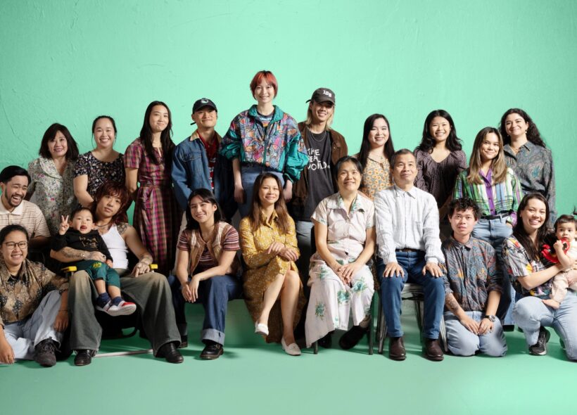 Very big cheerful group portrait of Vietnamese family and friends, all smiling against a green background 